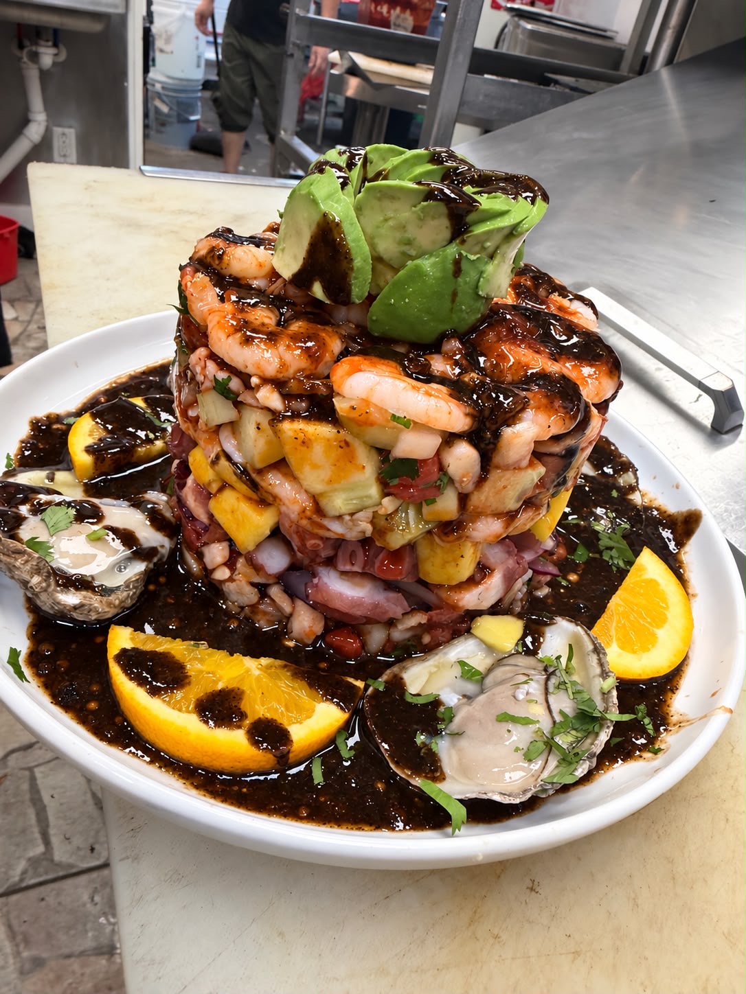 Tower of shrimp, octopus and ceviche layered with mango and avocado, drizzled with black salsa negra, served with oysters and citrus