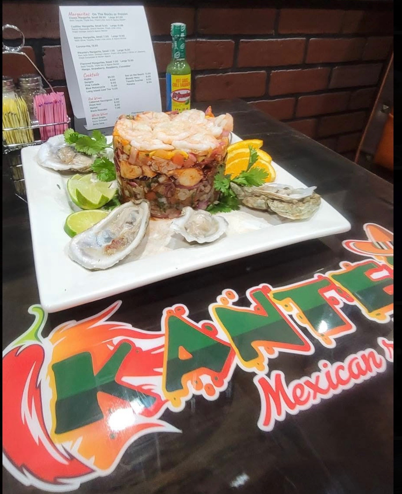 Tower of mixed ceviche and shrimp topped with shrimp ring, served with raw oysters, lime and orange