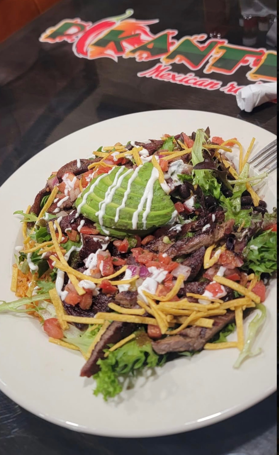 Carne asada salad with sliced avocado, black beans, pico de gallo, cheese and crema over fresh greens