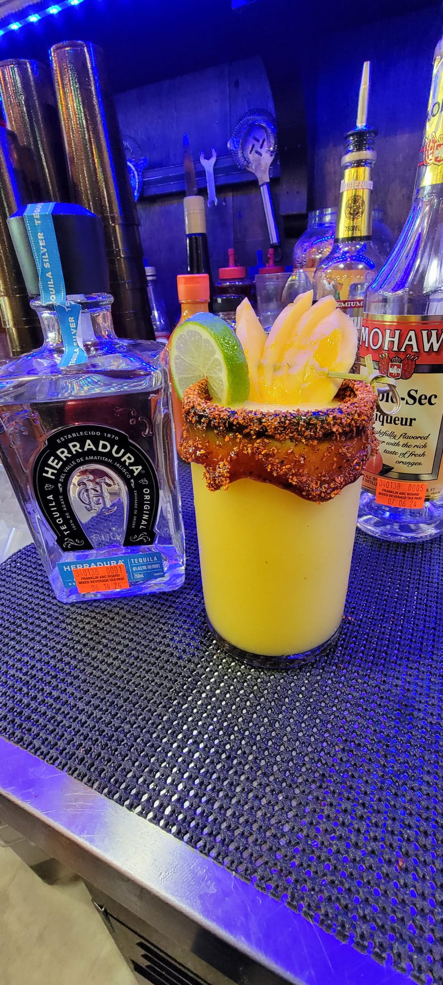 Mango margarita with chili-chamoy rim garnished with fresh mango slices and lime