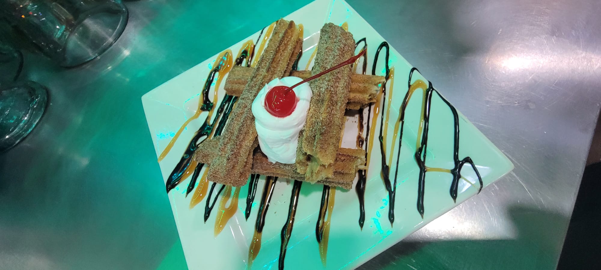 Churros dessert with whipped cream, cherry, caramel and chocolate drizzle