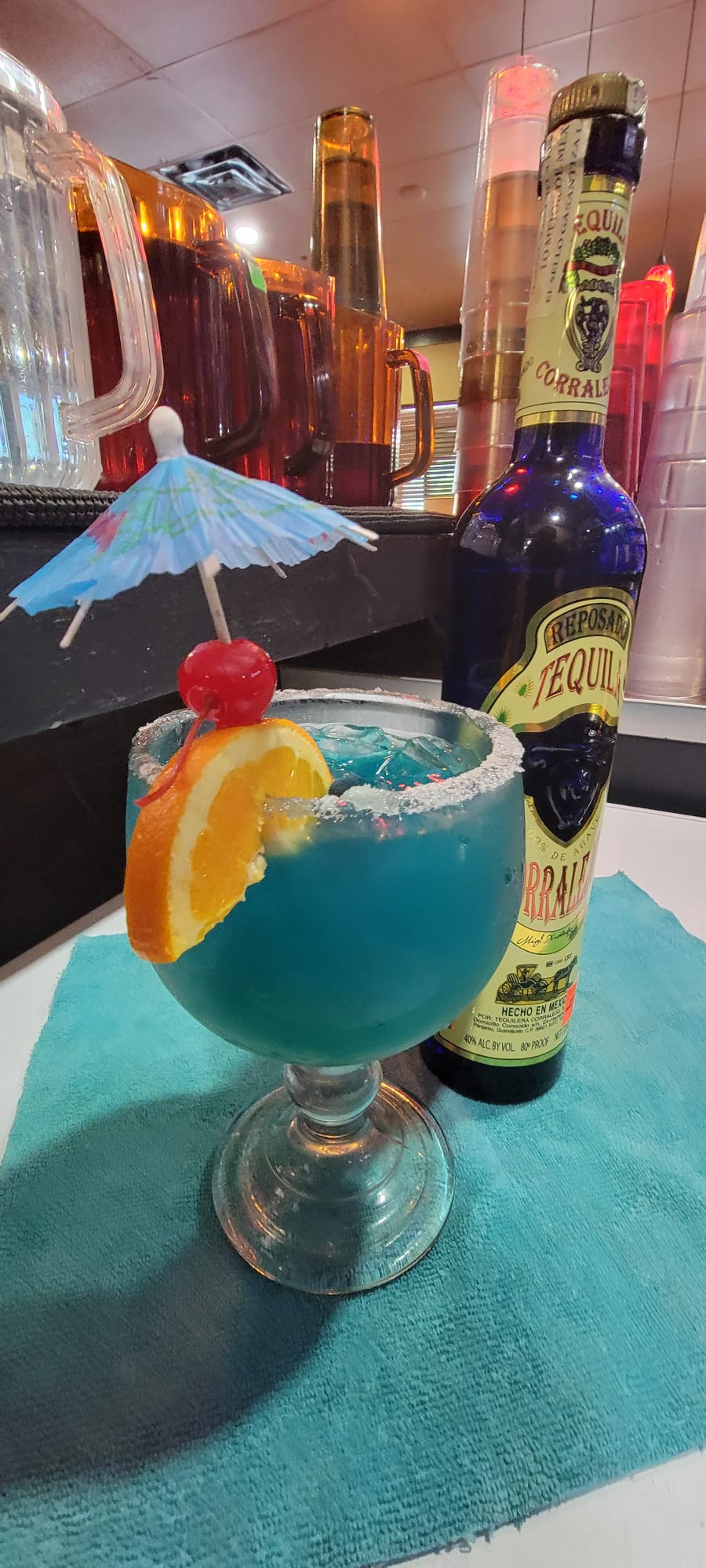 Blue margarita in a salted goblet garnished with orange slice, cherry and paper umbrella